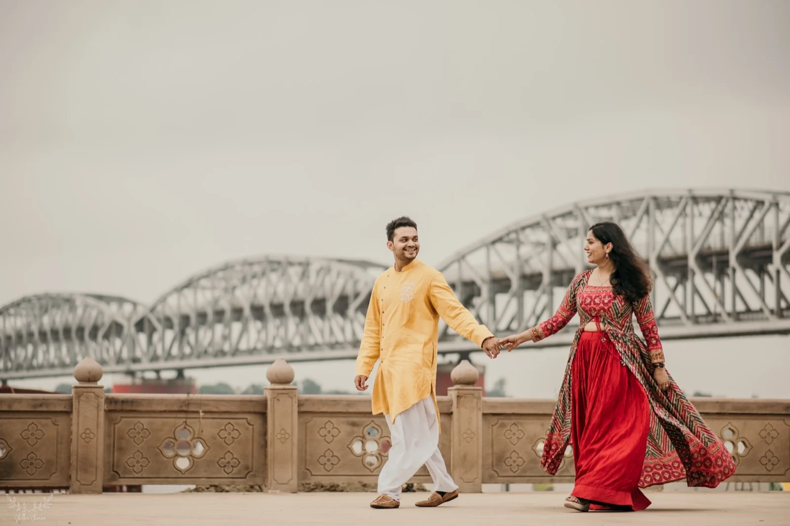 Couple walking hand in hand by riverside bridge during pre-wedding shoot