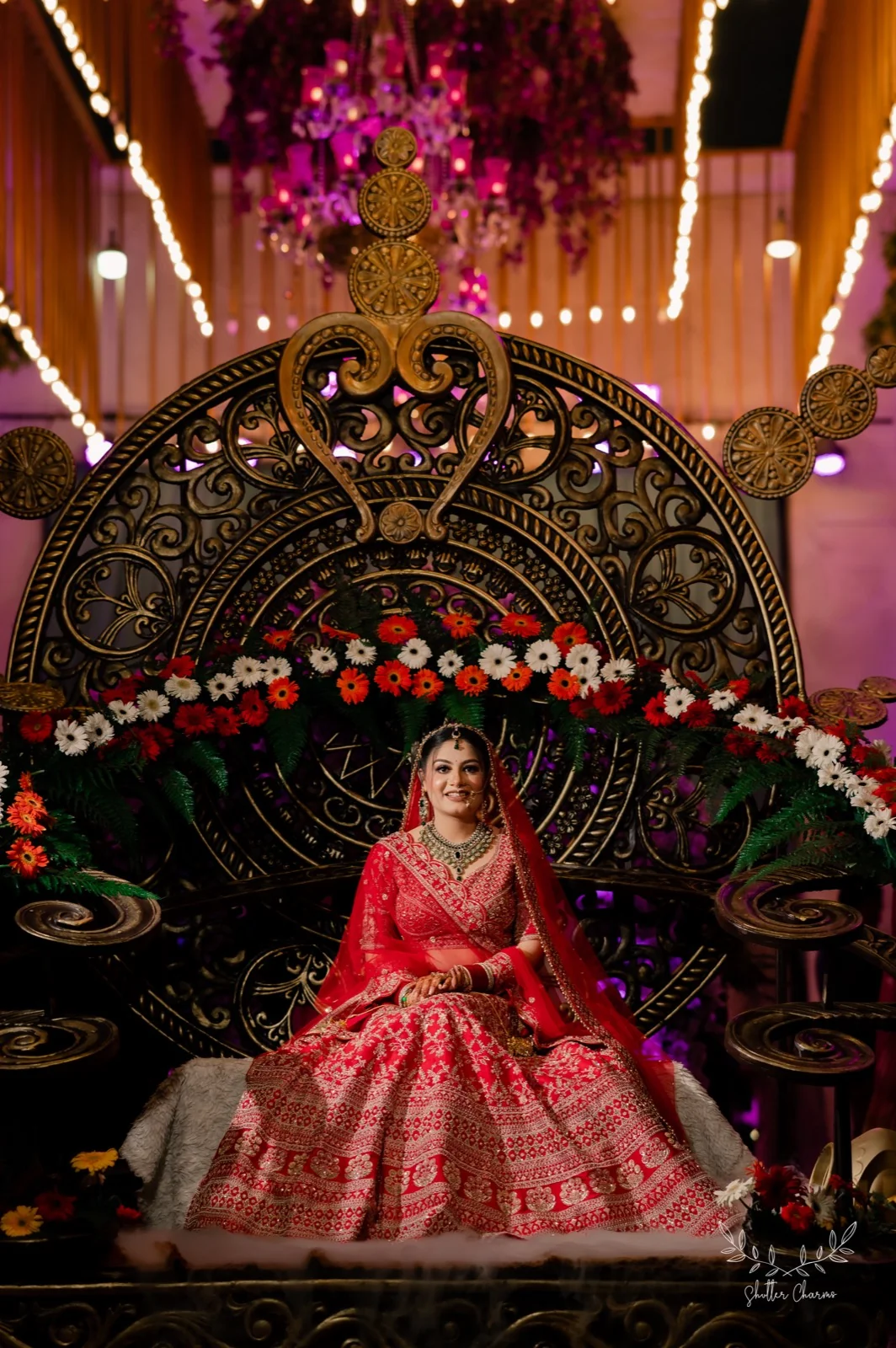 Bride in red lehenga seated on an ornate golden throne