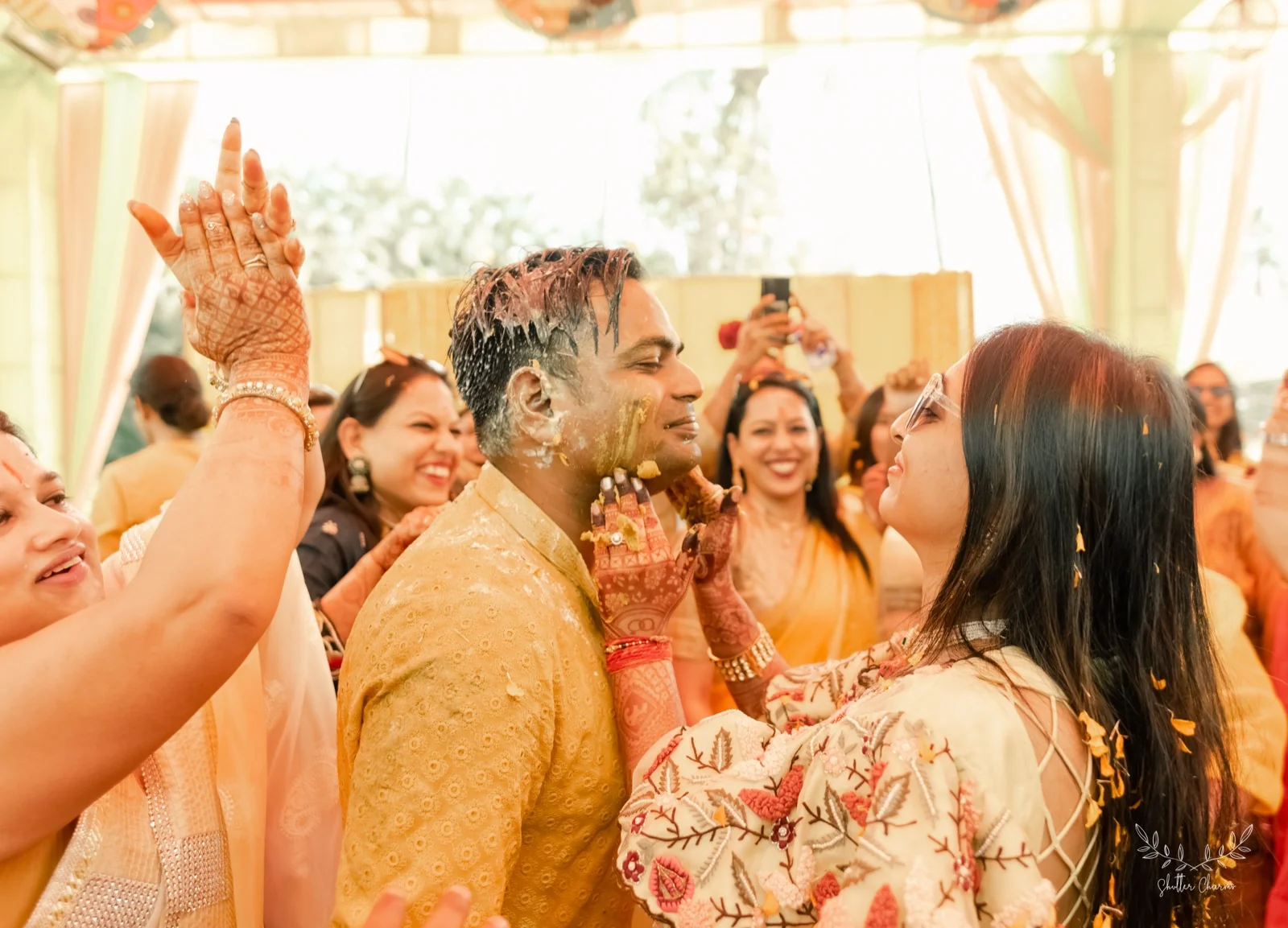 Family joyfully applying haldi to the groom's face
