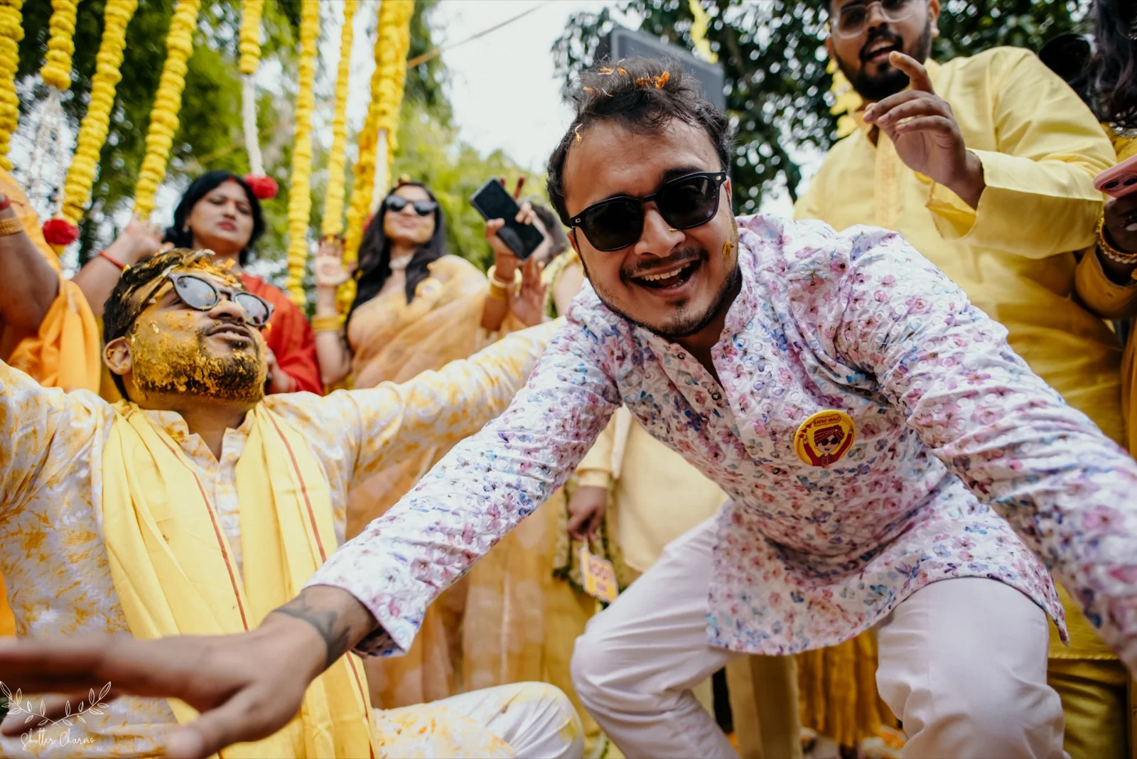 Groomsmen dance joyfully under marigold garlands at the haldi
