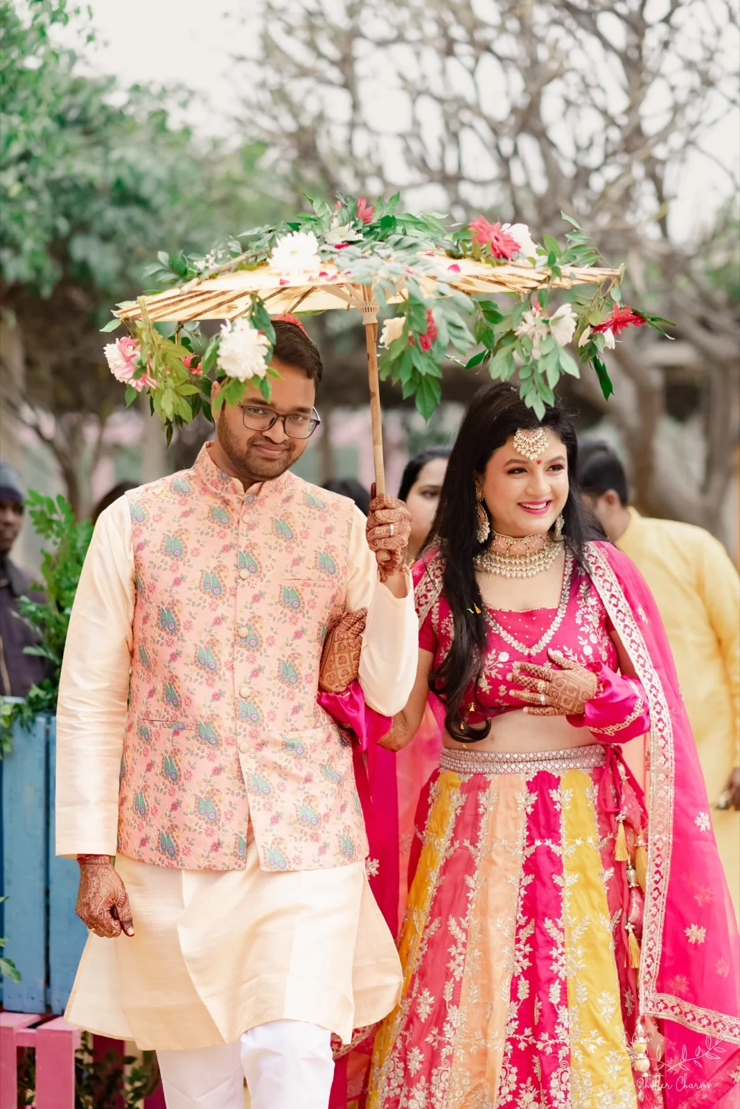 Couple under a floral umbrella arriving at their mehendi celebration