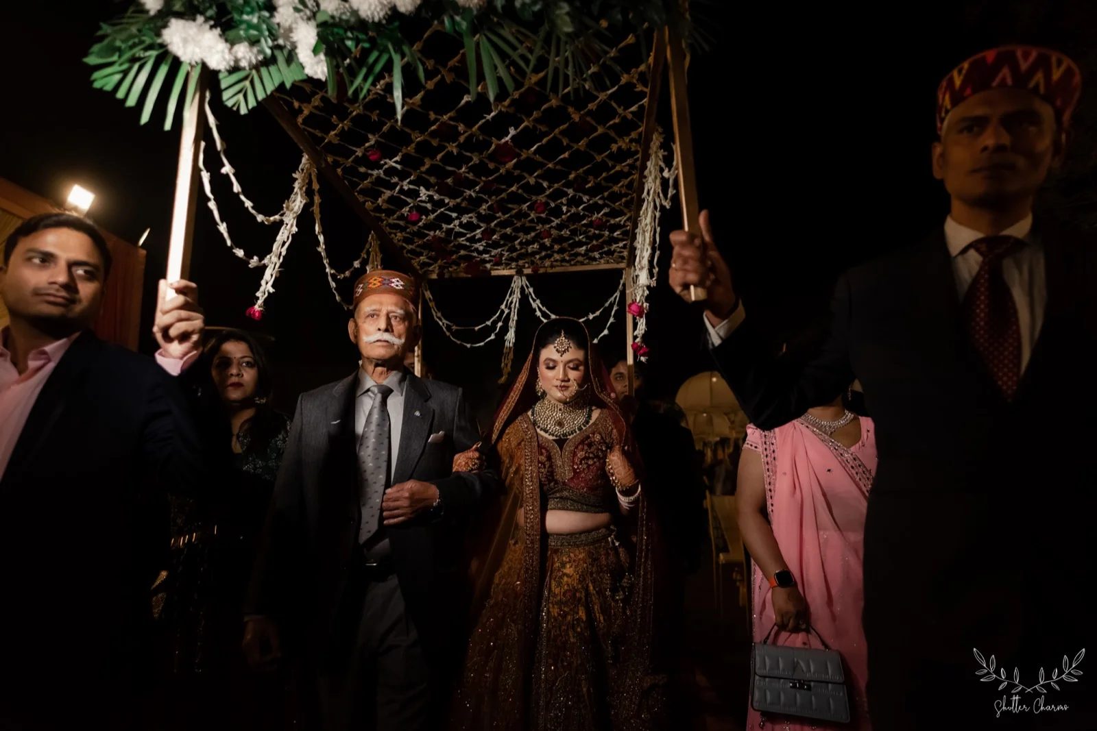 Bride enters under a floral canopy escorted by family elders