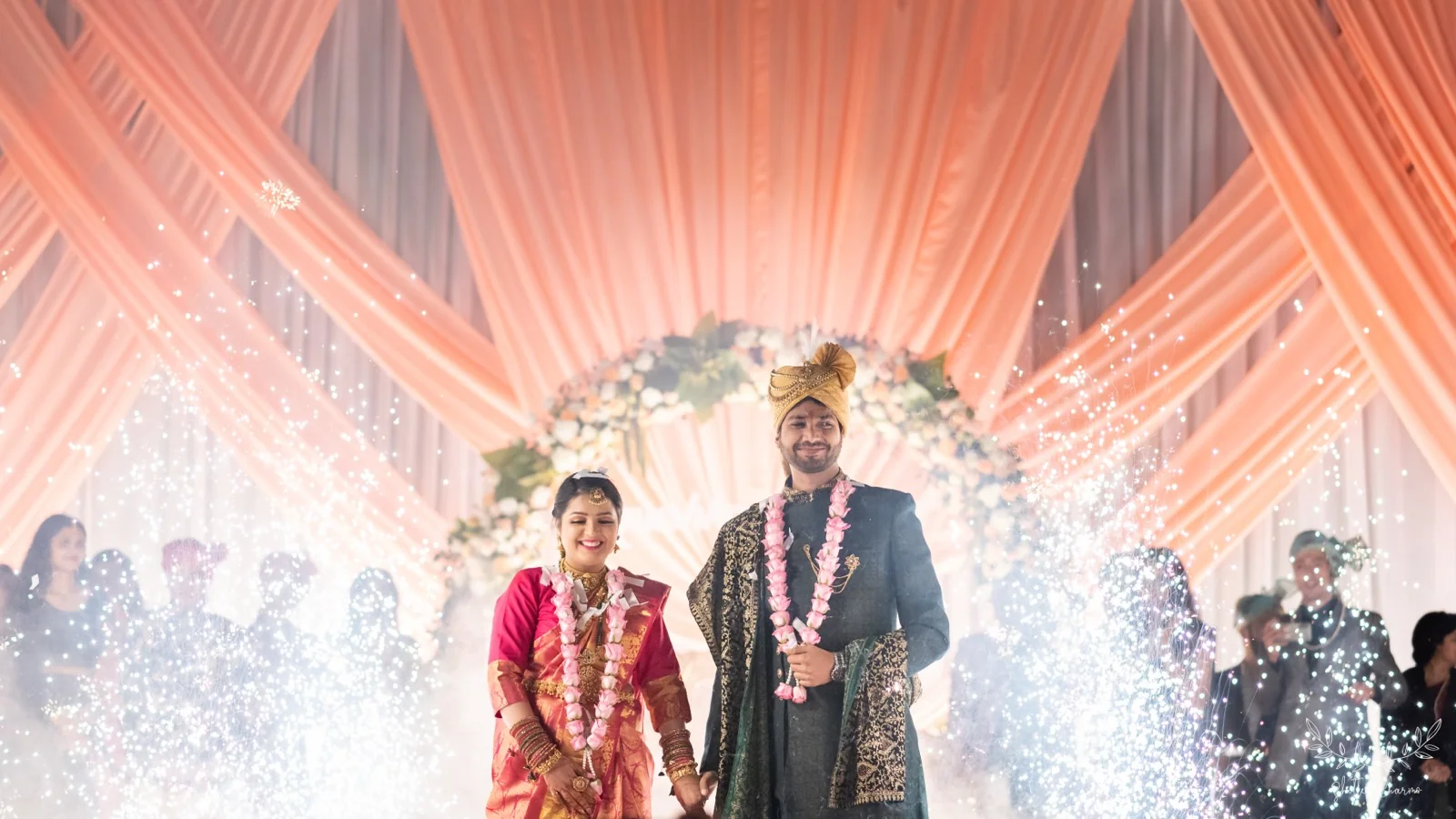 Garlanded bride and groom on stage amid sparkling cold pyros