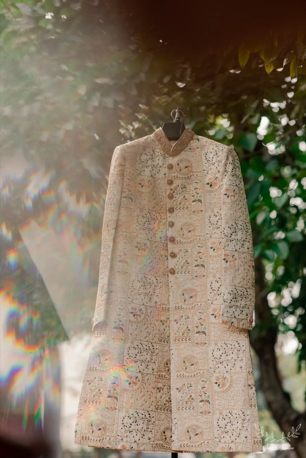 Groom's embroidered ivory sherwani hanging outdoors among green leaves