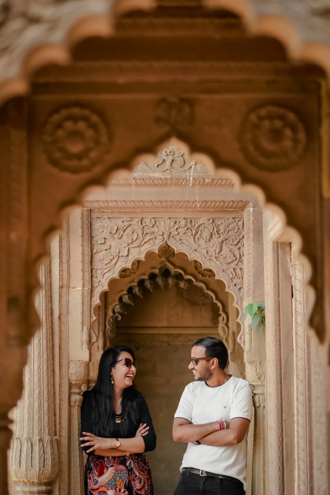 Couple laughing together under carved sandstone arches during pre-wedding shoot