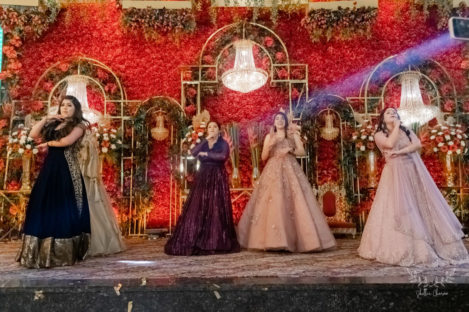 Women performing a choreographed sangeet dance on a floral stage